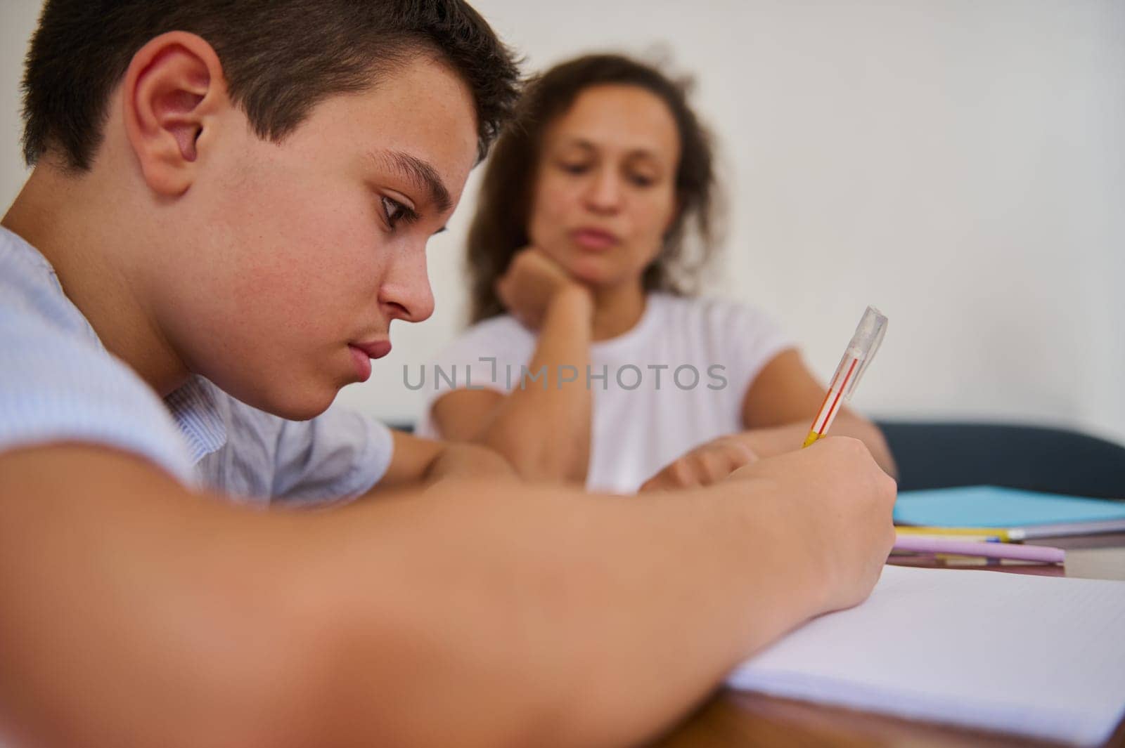 A young student concentrating on writing while a tutor observes attentively. The scene depicts a supportive learning environment, highlighting focus, education, and guidance. Ideal for themes of tutoring, student learning, and mentorship.
