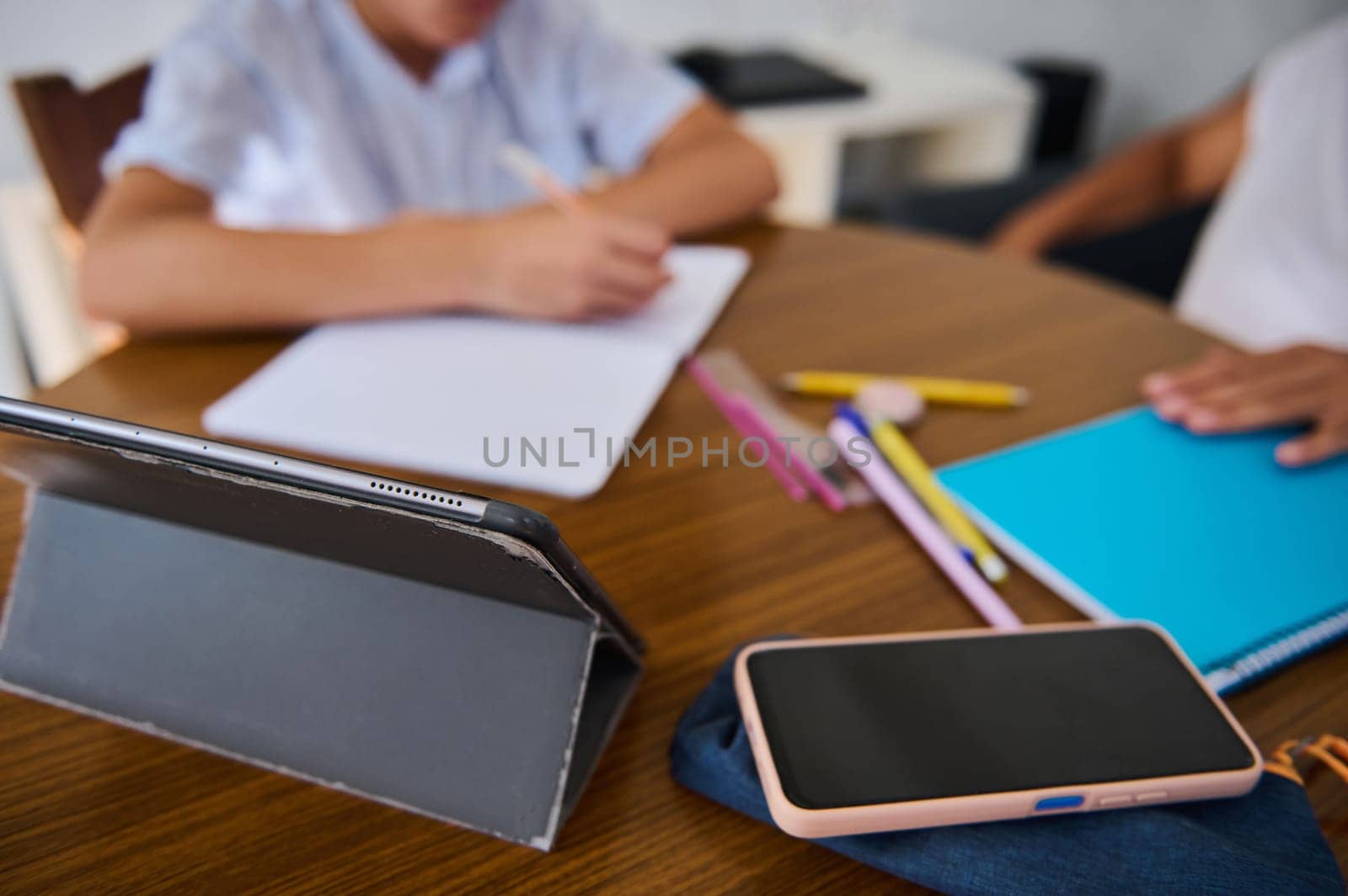 Students engaged in digital learning with tablets and notebooks. Close-up of a modern workspace setup with writing materials, fostering a productive education environment.