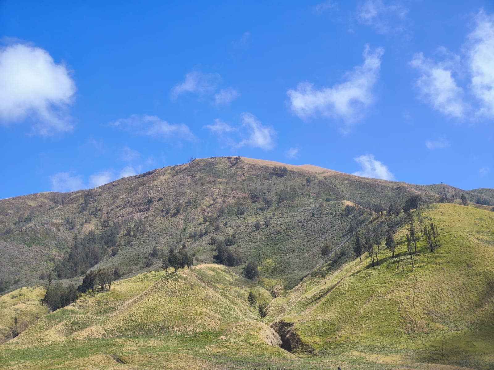 A picturesque landscape of rolling hills with vibrant green grass under a dramatic blue sky and fluffy white clouds.