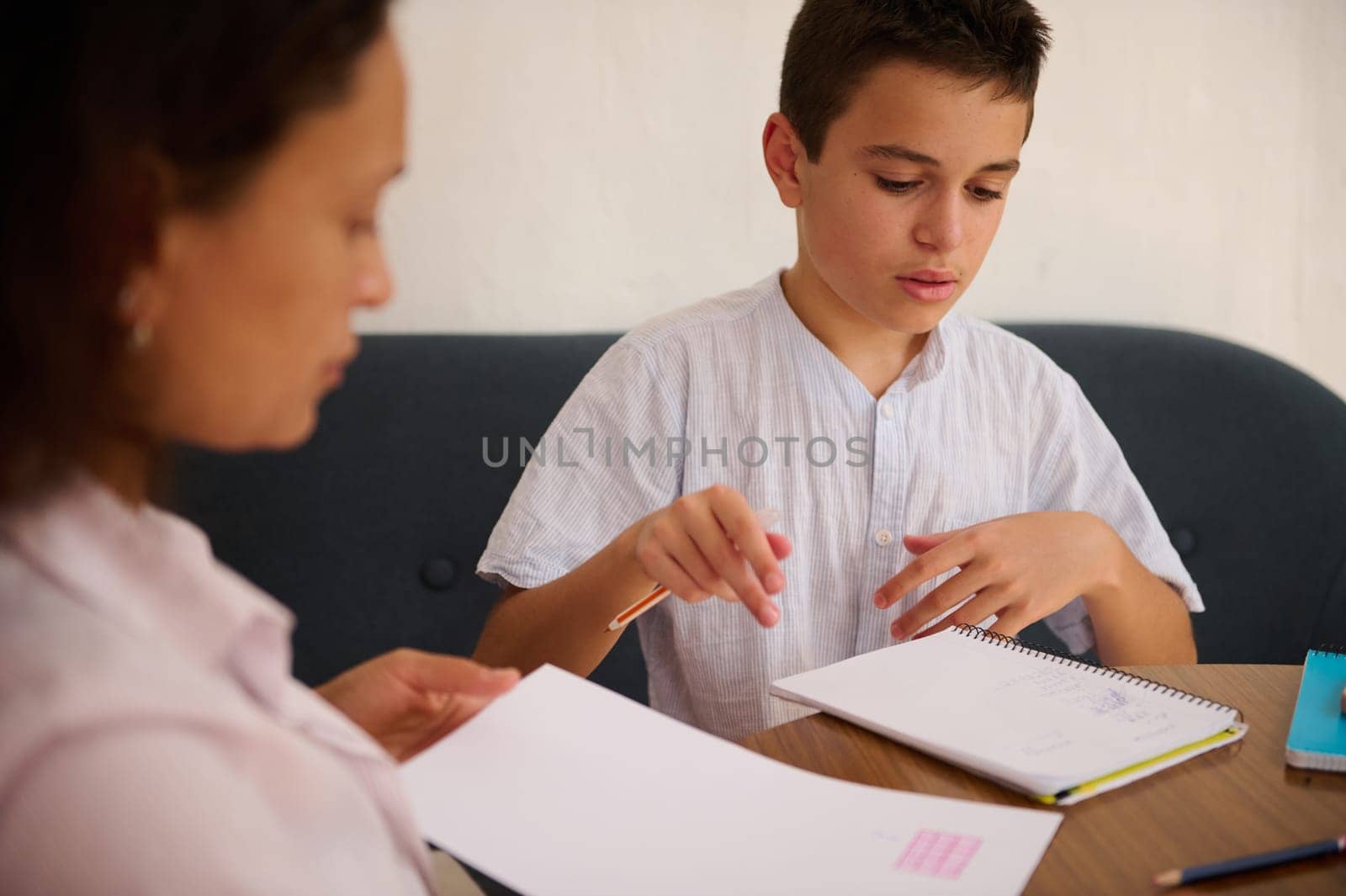 A mother guides her son through a focused homeschool lesson, emphasizing education and dedication. They are engaged with open books, fostering a supportive learning environment.