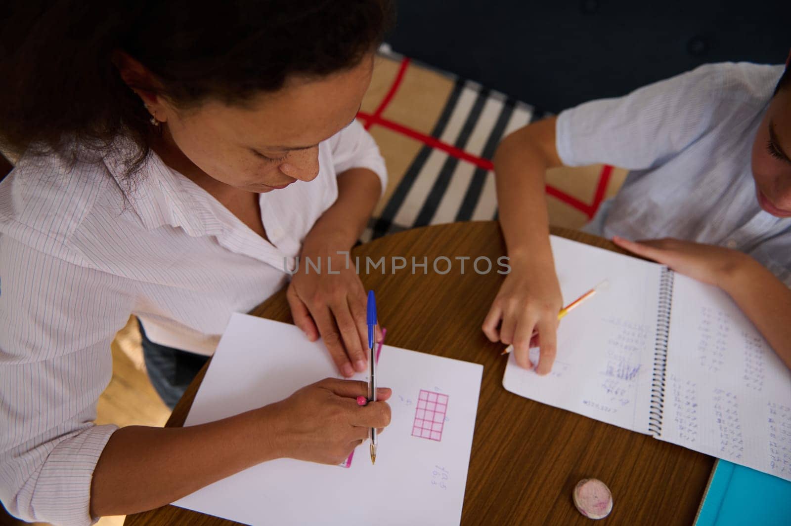 A mother assists her child with math homework at a wooden table, fostering learning and support in a cozy home environment, illustrating family education and togetherness.