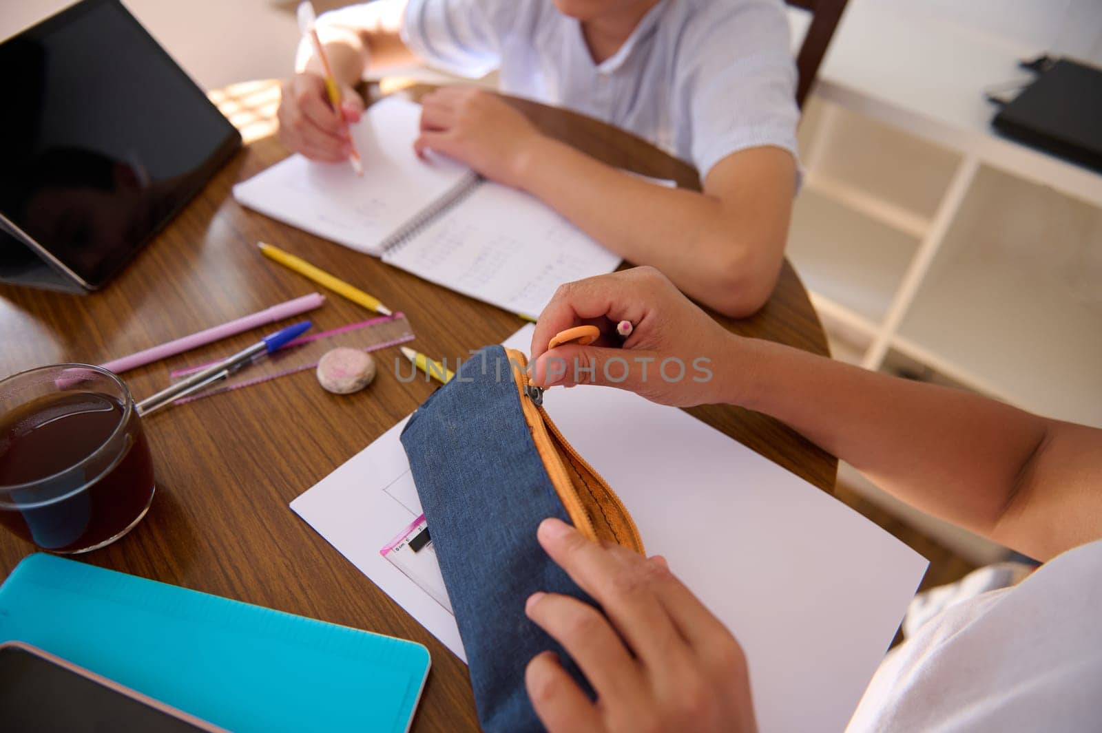 Two children study together, focusing on writing and drawing. The image conveys teamwork, learning, and concentration at a wooden table equipped with school supplies and a digital tablet.