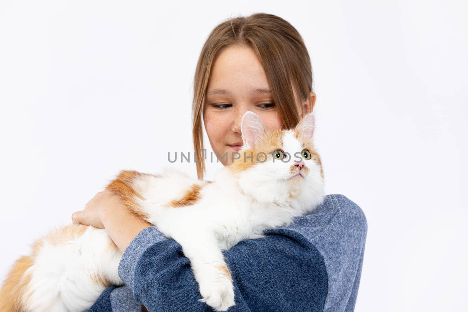 A girl joyfully holds a fluffy ginger cat against a bright background, showcasing their beautiful bond