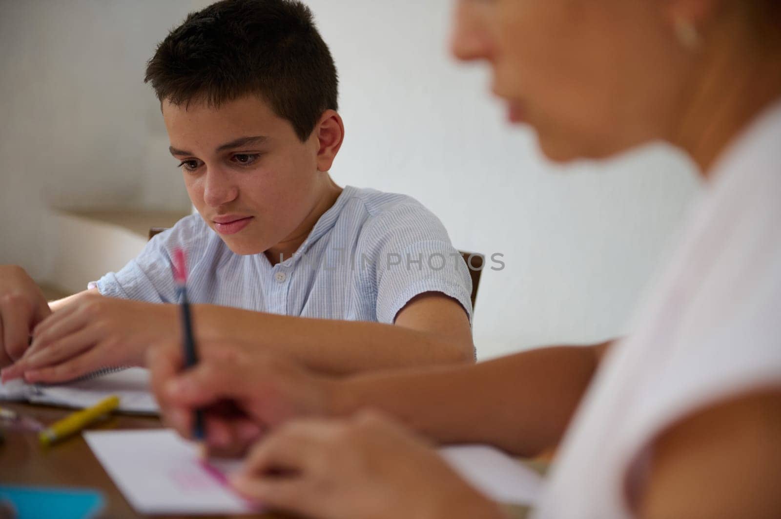 A focused young boy works on homework with an adult in a supportive study environment, emphasizing education and teamwork.