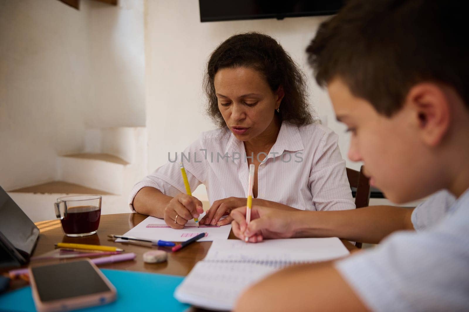 A mother and her son are focused on studying together at home, surrounded by study materials. Their teamwork reflects a supportive and educational environment.