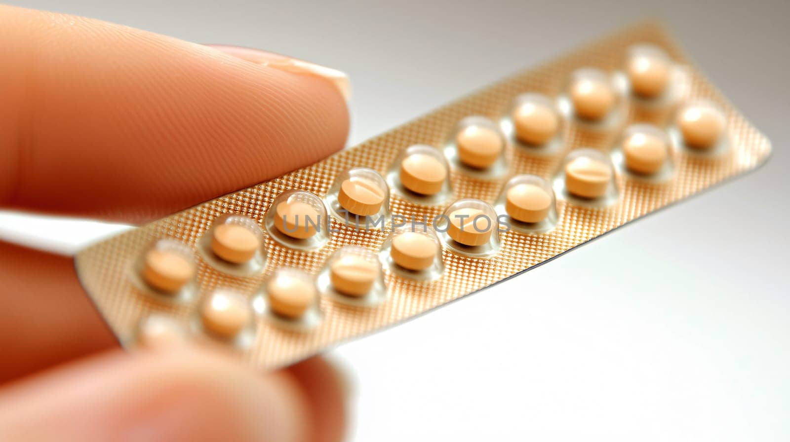 Woman is holding a blister pack of contraceptive pills between her fingers