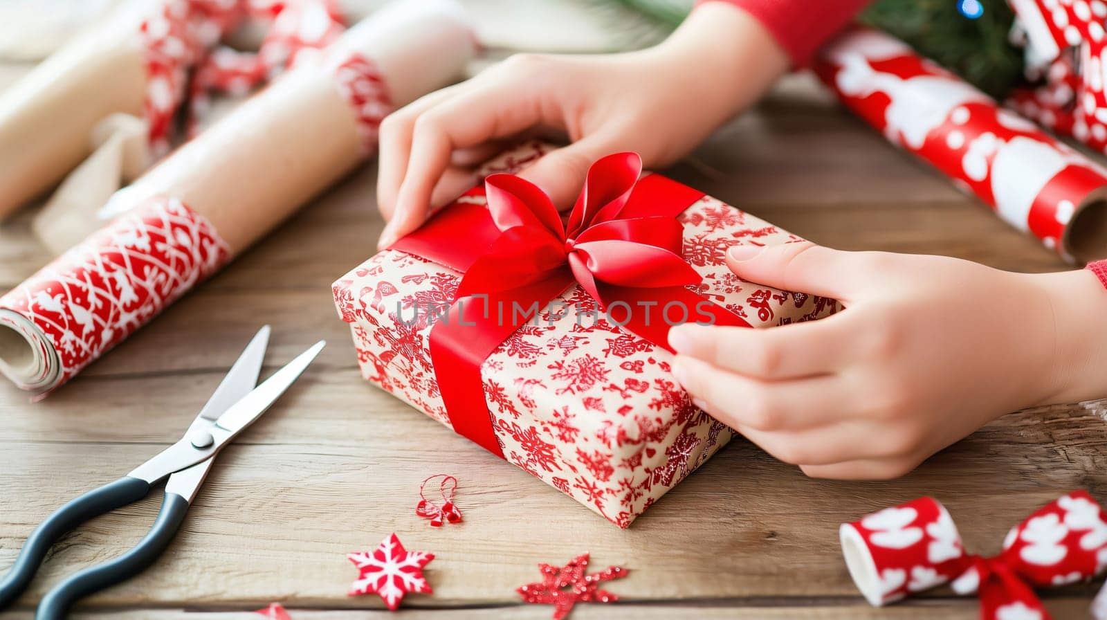 Woman is wrapping a christmas present with red ribbon on a wooden table