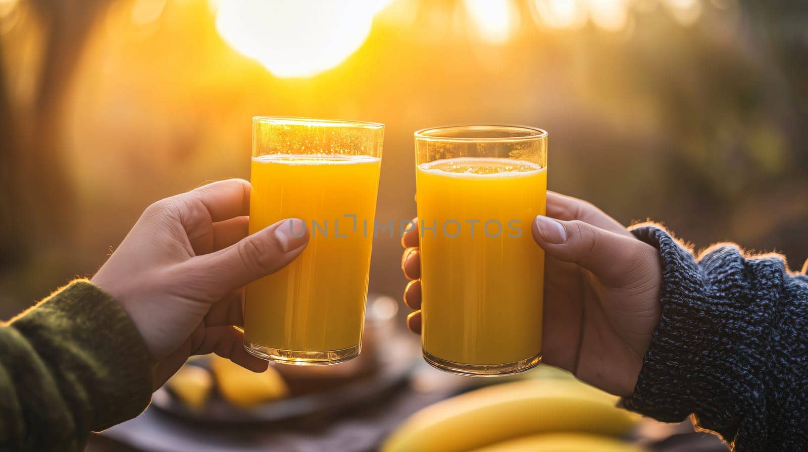 Two people are holding orange juice glasses during a sunrise breakfast picnic