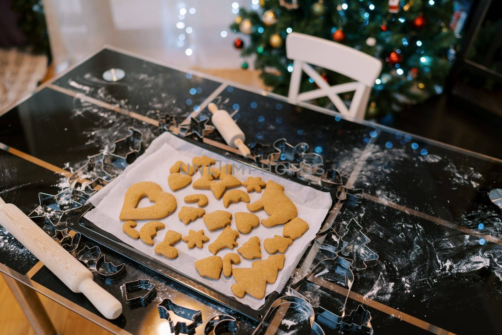 Tray with baked gingerbread cookies stands on a table near a decorated Christmas tree. High quality photo