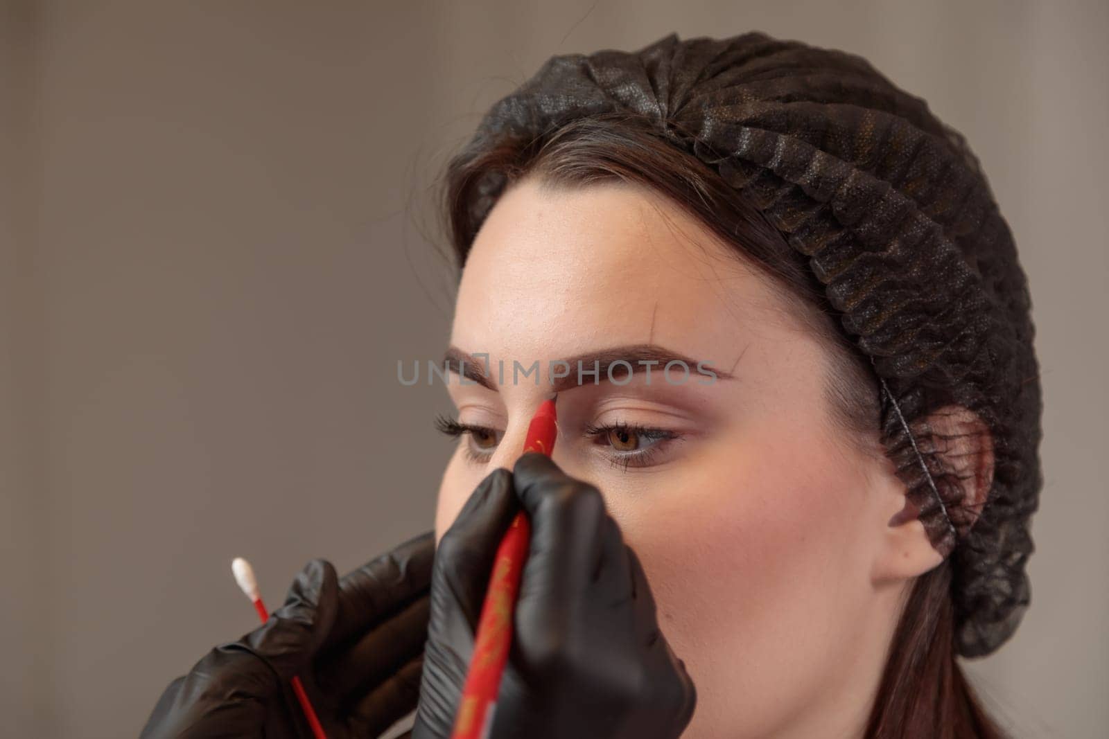 Beautician preparing a woman for microblading treatment, drawing eyebrow shape on her face