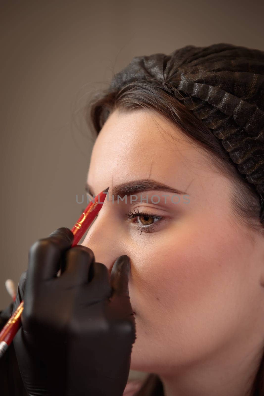 Beautician preparing eyebrows for permanent makeup by drawing lines with red pencil