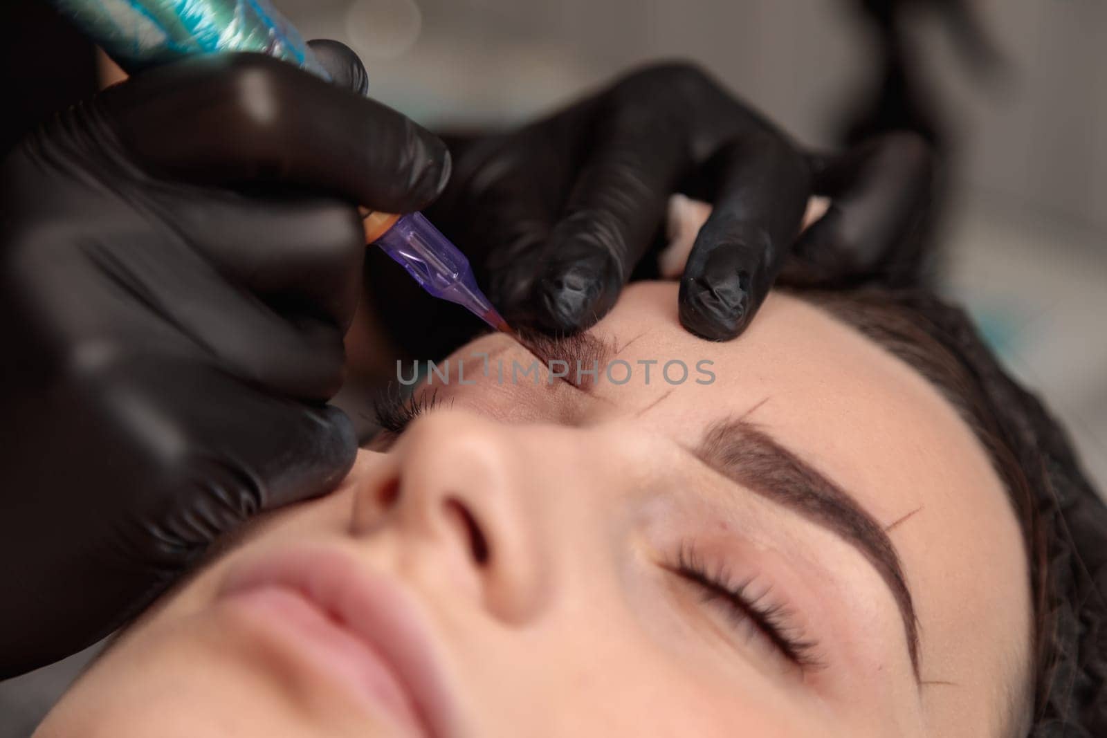 Beautician performing microblading procedure on eyebrows of client in beauty salon