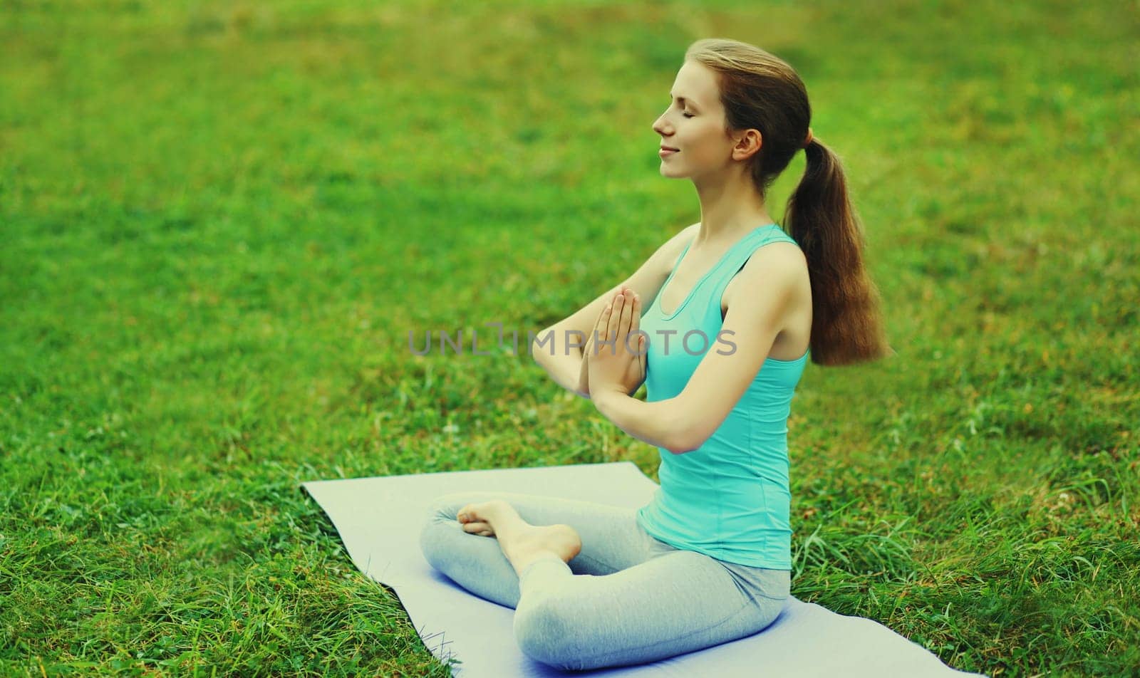 Young woman doing yoga exercises on a mat on the grass in summer park