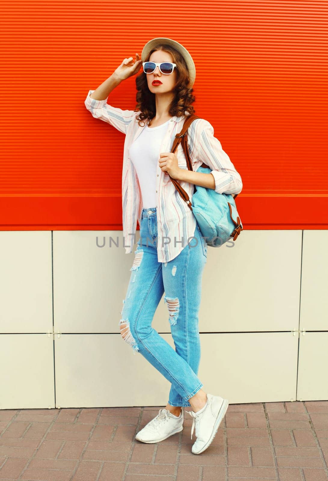 Young woman model posing wearing a casual, summer straw round hat on city street over red background