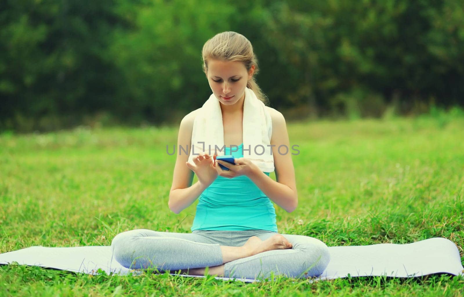 Fitness woman with smartphone on a mat on the grass in summer park