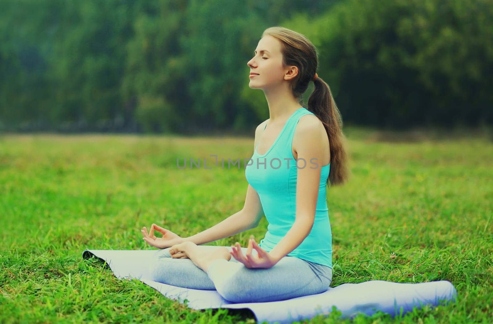 Young woman doing yoga exercises on a mat on the grass in summer park