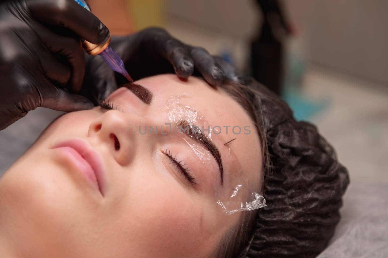 Beautician is making permanent eyebrow makeup for a client in a beauty salon