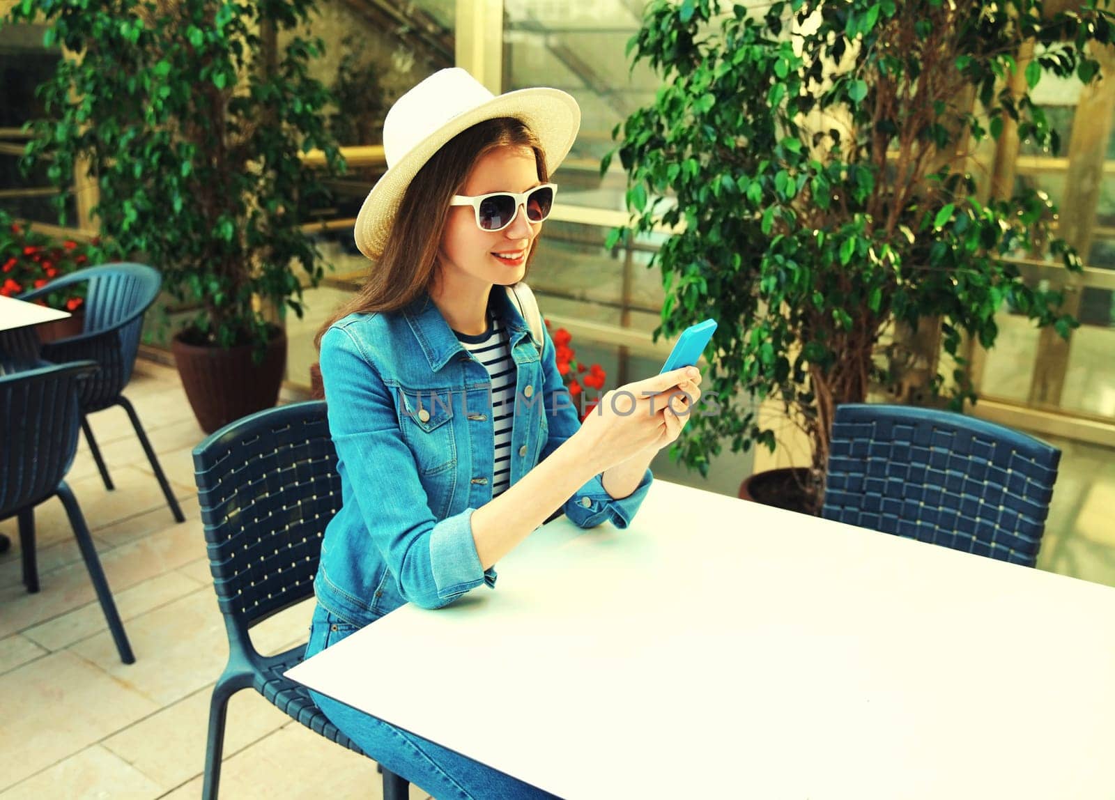 Portrait of smiling young woman sitting at table in cafe with phone