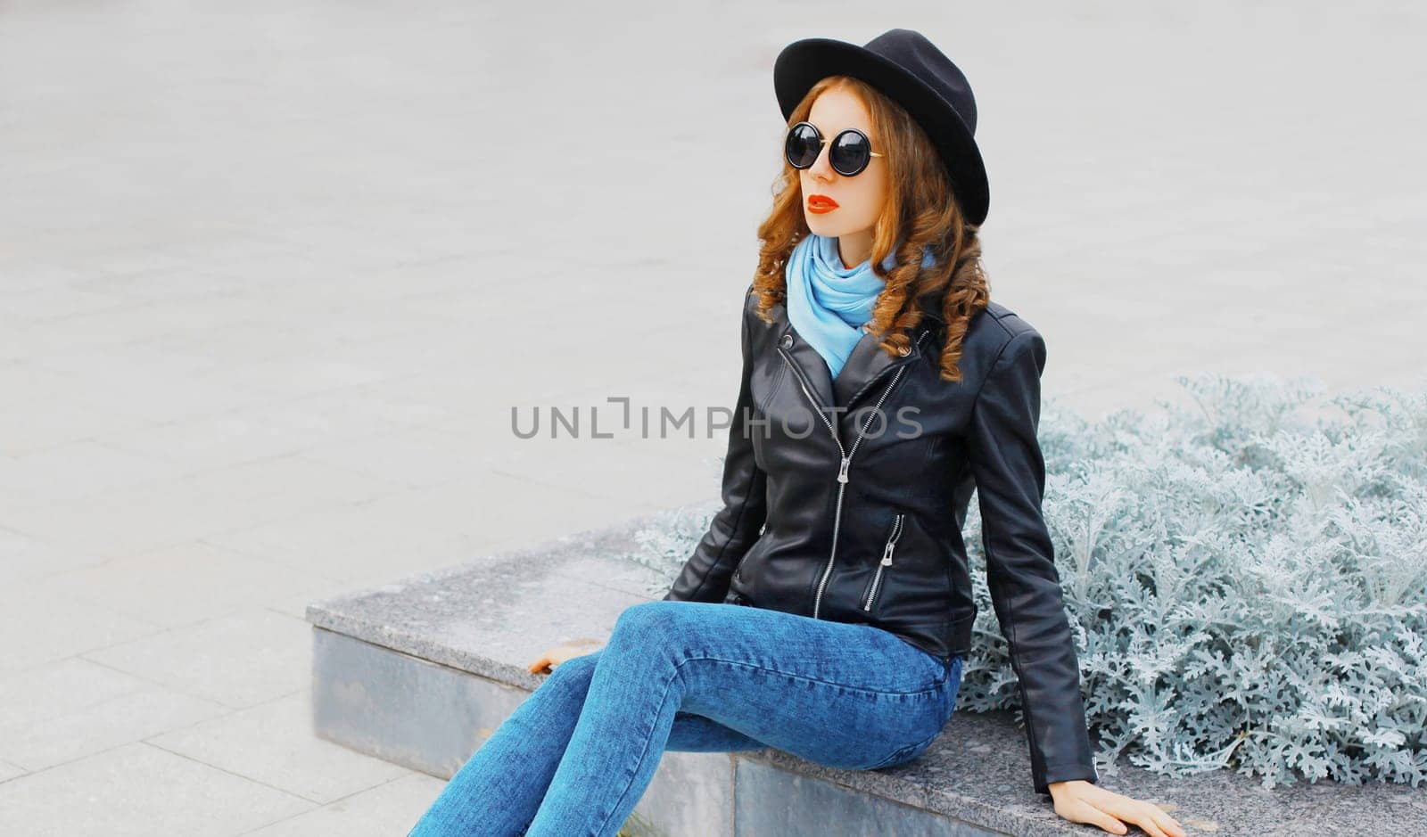Fashion young woman posing in black rock jacket, hat at city park