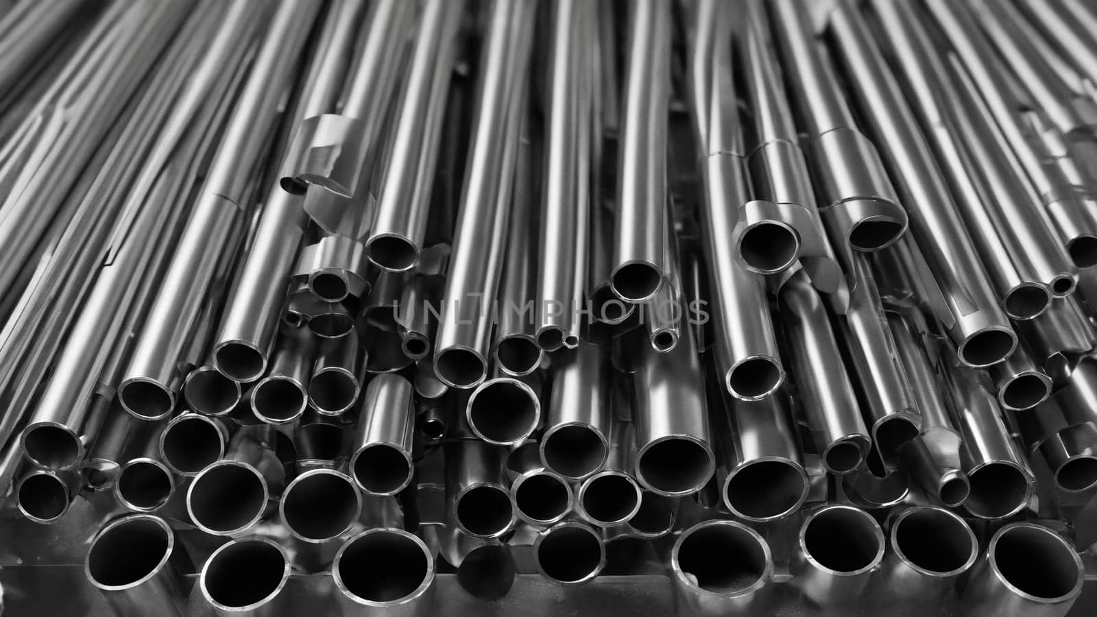 A collection of shiny metal pipes lies stacked, their surfaces gleaming subtly under diffused daylight. The cool atmosphere enhances the industrial vibe of the setting.