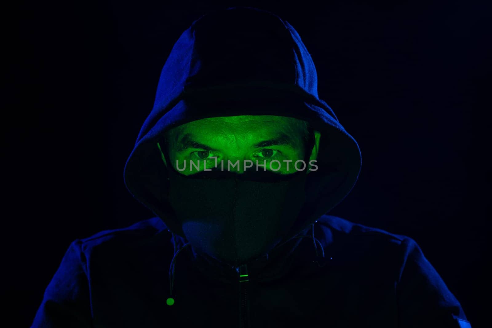Short of computer hacker wearing white mask stealing data from a laptop. Masked hacker using laptop computer for organizing massive data breach attack on corporate servers in neon room.