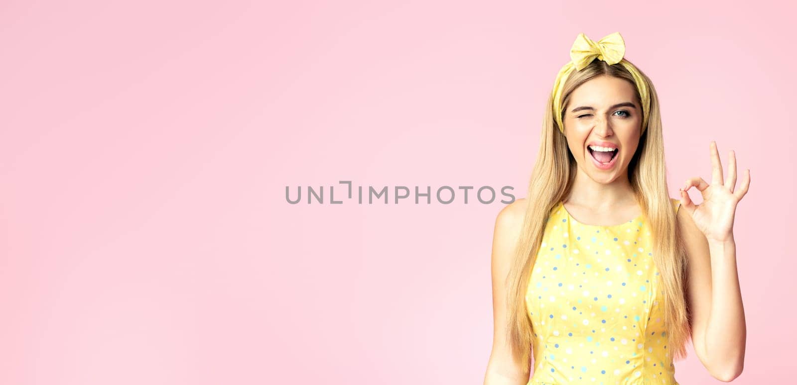 I'm Fine. Smiling blonde woman showing ok sign, winking and looking at camera isolated over pink wall, copyspace