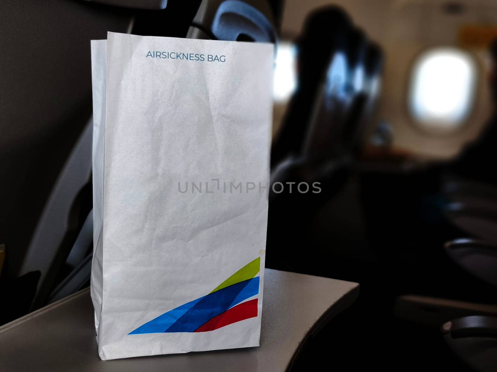An airsickness bag with a colorful airline logo rests on an airplane seatback tray.