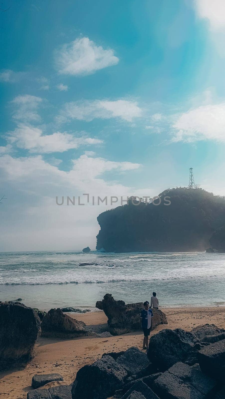 A rocky shoreline with a large rock formation in the background. The water is calm and the sky is blue
