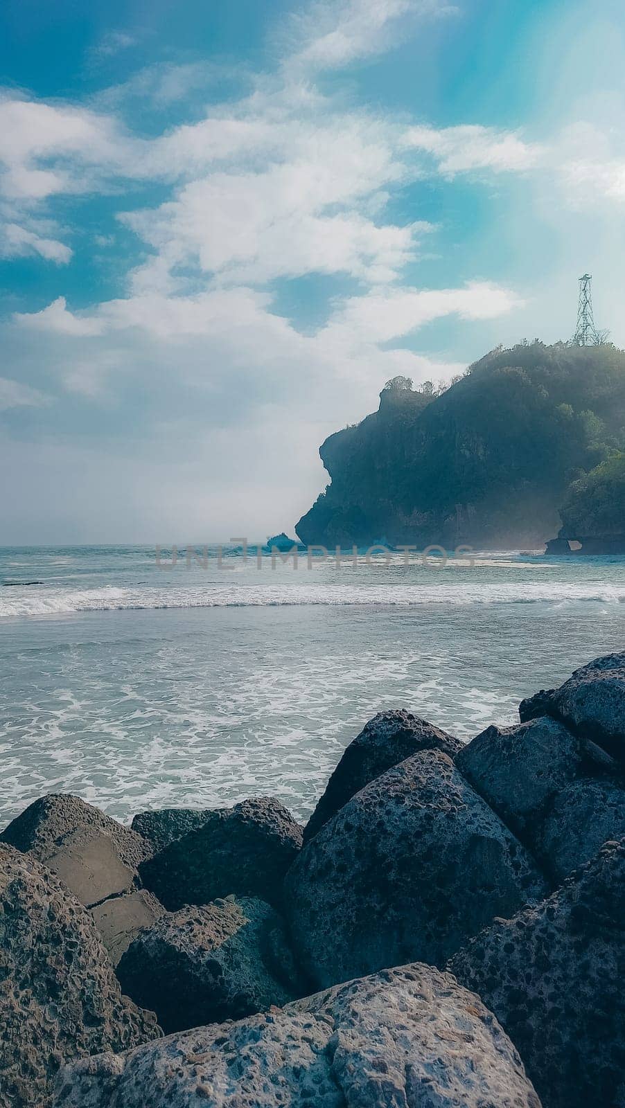 A rocky shoreline with a large rock formation in the background. The water is calm and the sky is blue