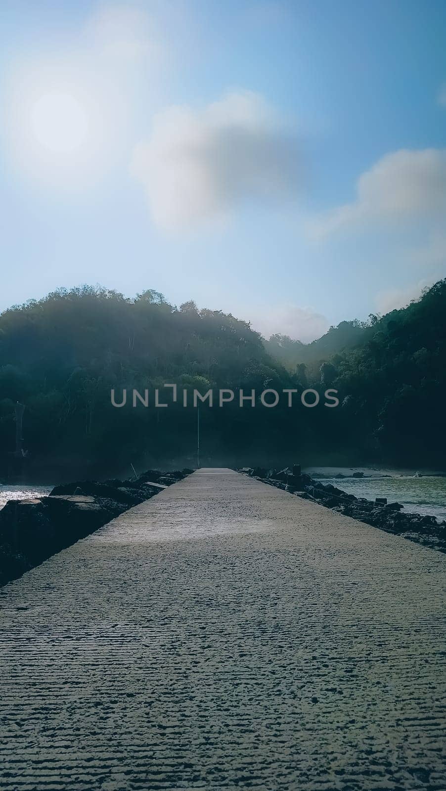 A rocky shoreline with a large rock formation in the background. The water is calm and the sky is blue