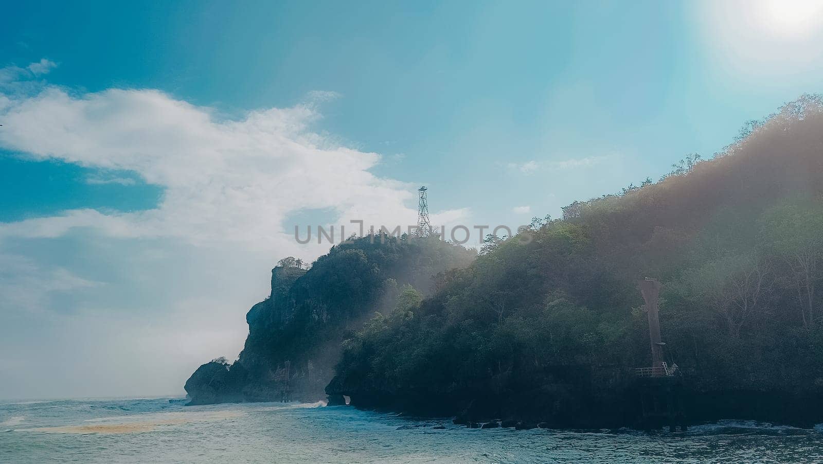 A rocky shoreline with a large rock formation in the background. The water is calm and the sky is blue