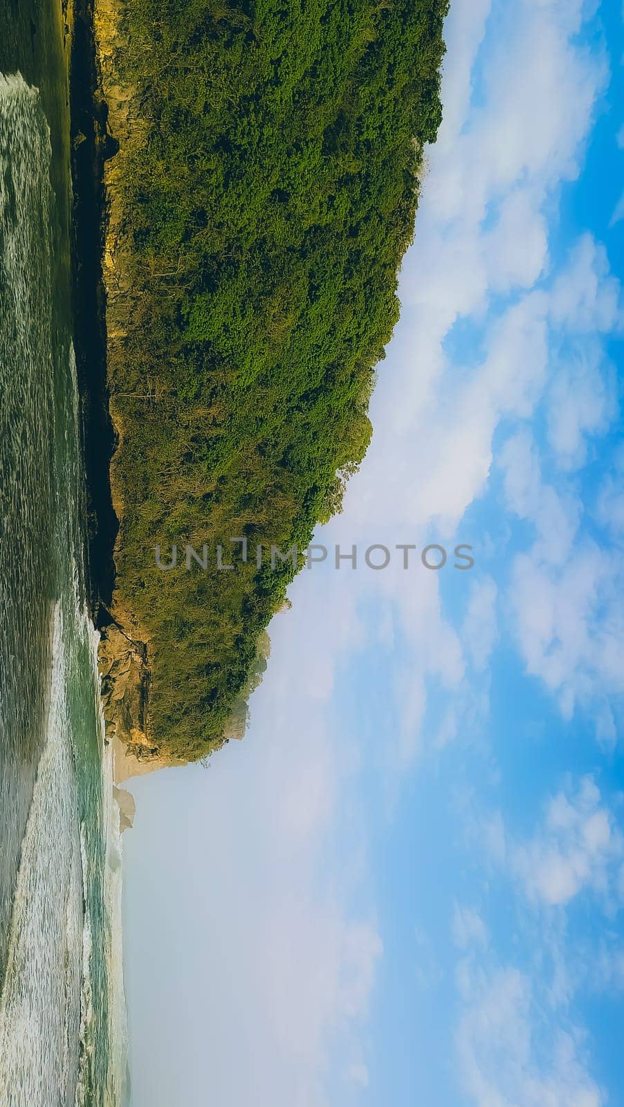 A rocky shoreline with a large rock formation in the background. The water is calm and the sky is blue
