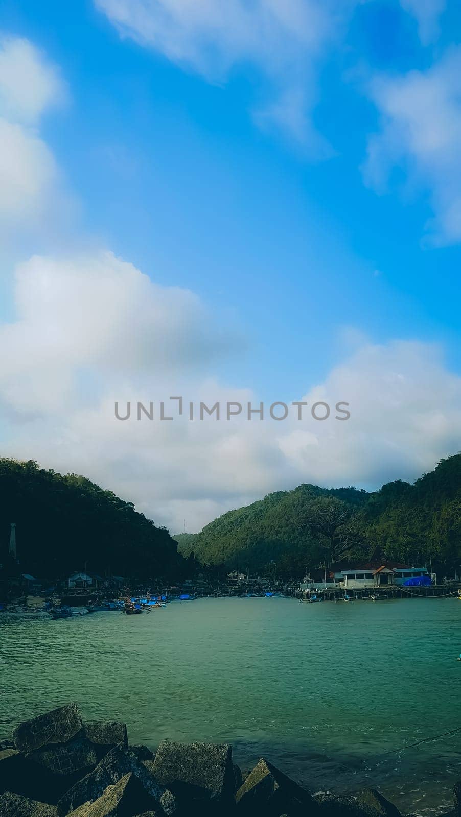 A rocky shoreline with a large rock formation in the background. The water is calm and the sky is blue