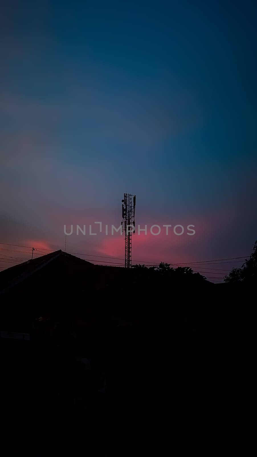 A silhouette of a communication tower stands prominently against a stunning pink and blue sky at sunset, evoking a sense of tranquility and modern technology.