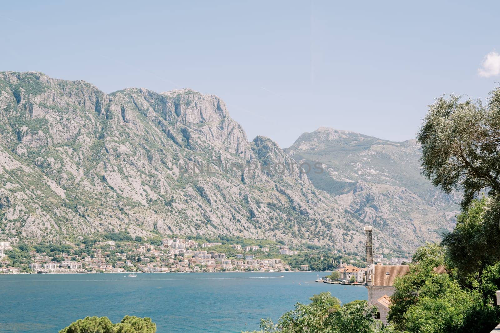 View over green tree branches and red roofs of houses on the sea with mountains in the background. High quality photo