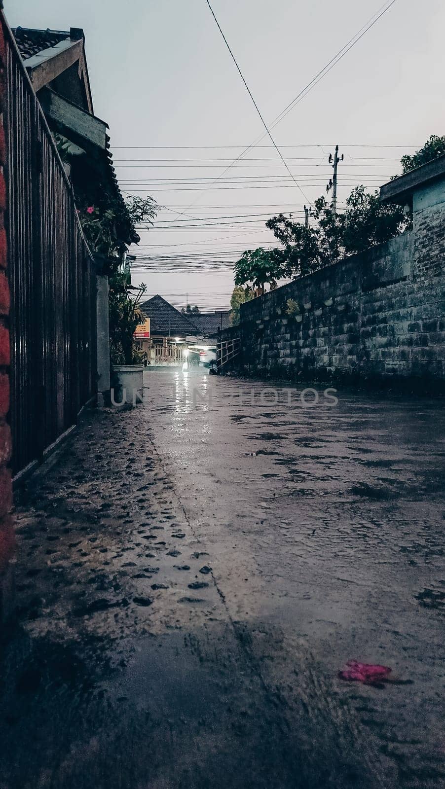 A tranquil urban street captured during a rainy evening, featuring wet pavement and dim lighting, conveying a peaceful and reflective atmosphere.