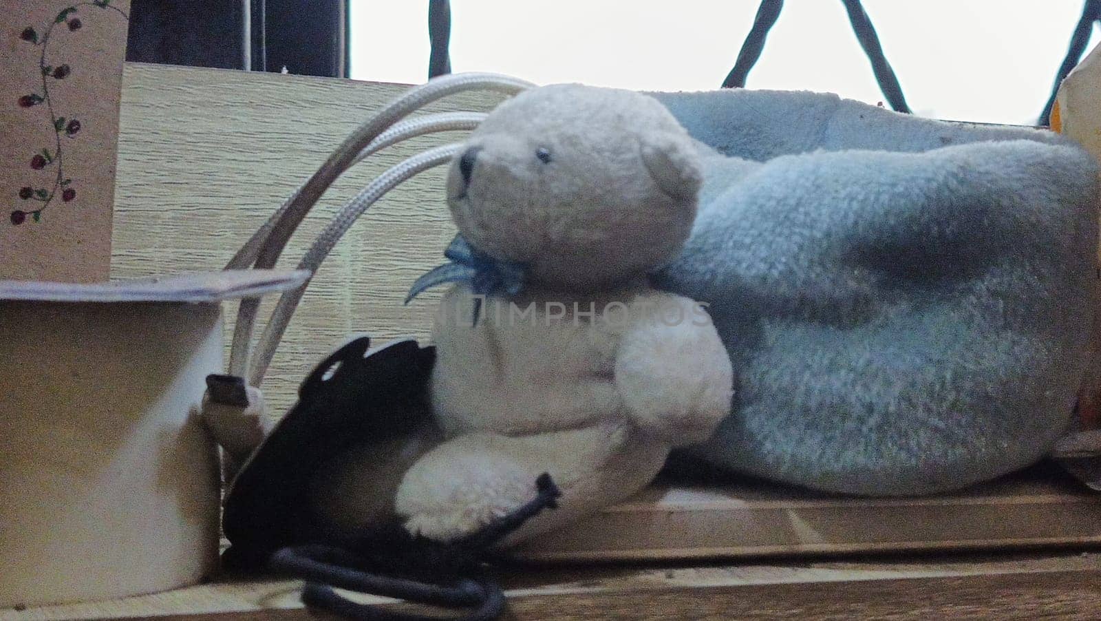 A teddy bear is sitting on a wooden surface next to a blue blanket. The scene is cozy and inviting, with the teddy bear looking up at the camera