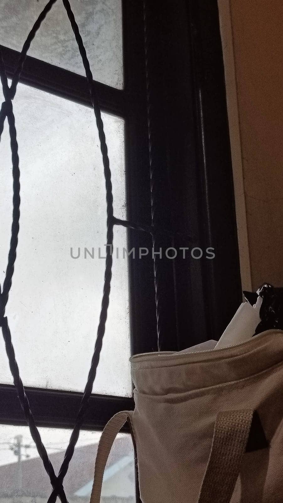 A window with a bag hanging from it. The bag is white and has a black strap