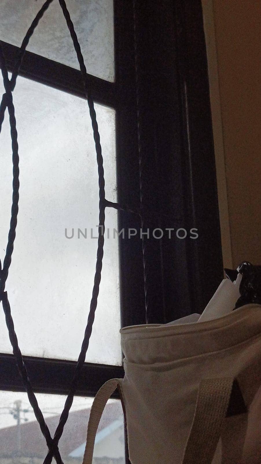 A window with a bag hanging from it. The bag is white and has a black strap