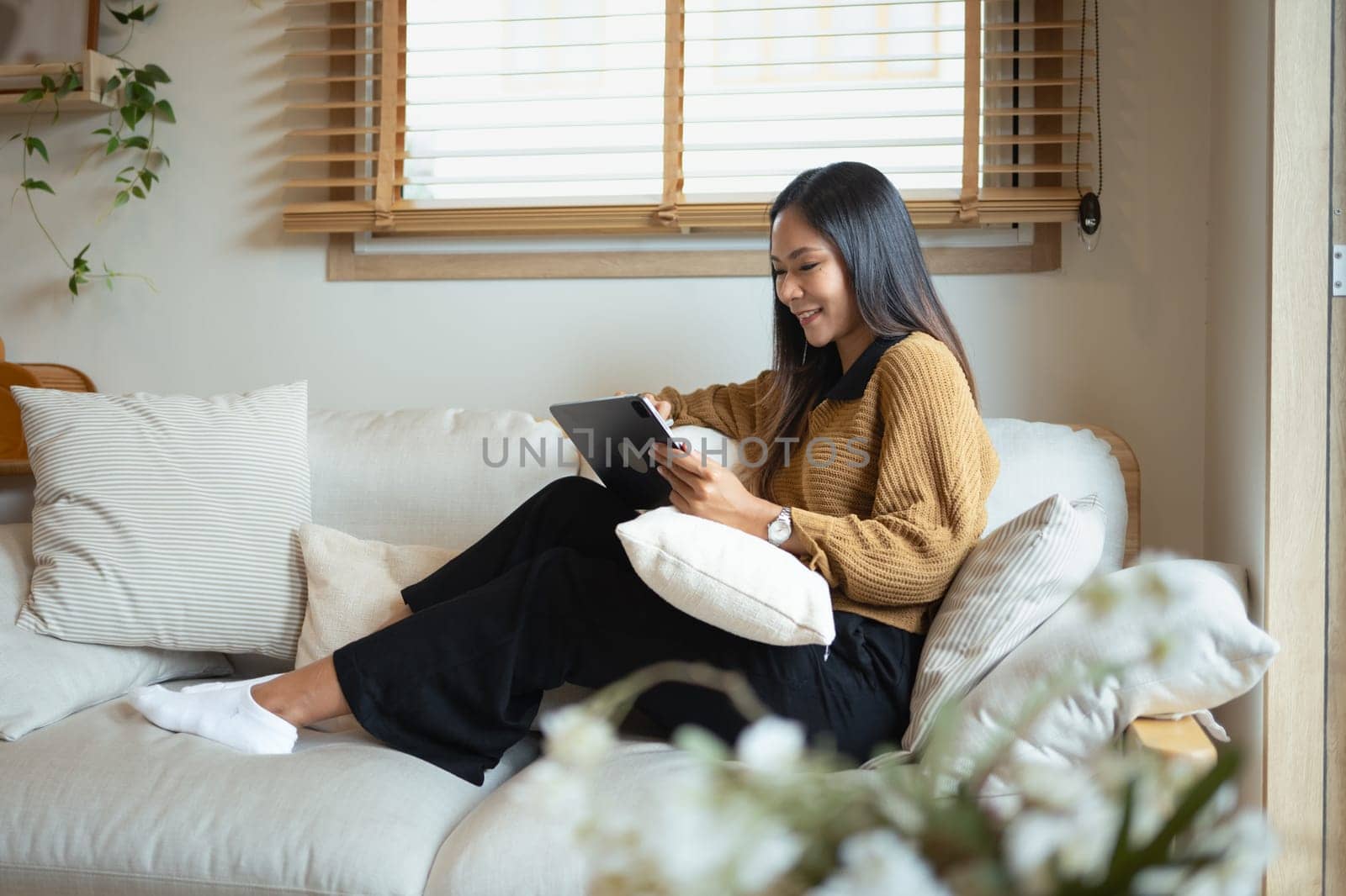 Charming young adult woman using digital tablet while relaxing on a cozy sofa.