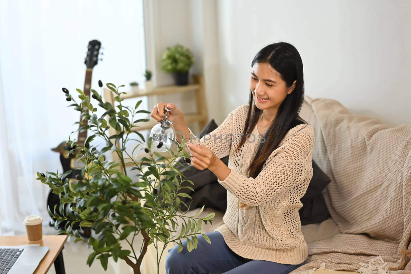 Young woman examining a potted plant in a living room. Home gardening and mindfulness concept.