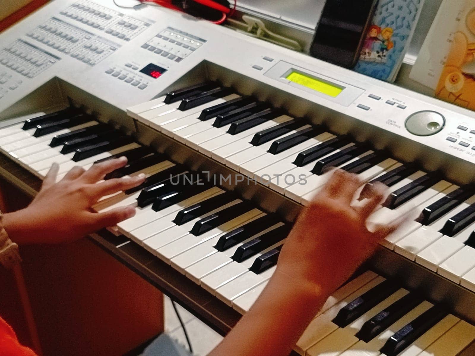 Close-up of young hands skillfully playing an electronic organ, capturing a moment of musical practice and creativity in a cozy music room.