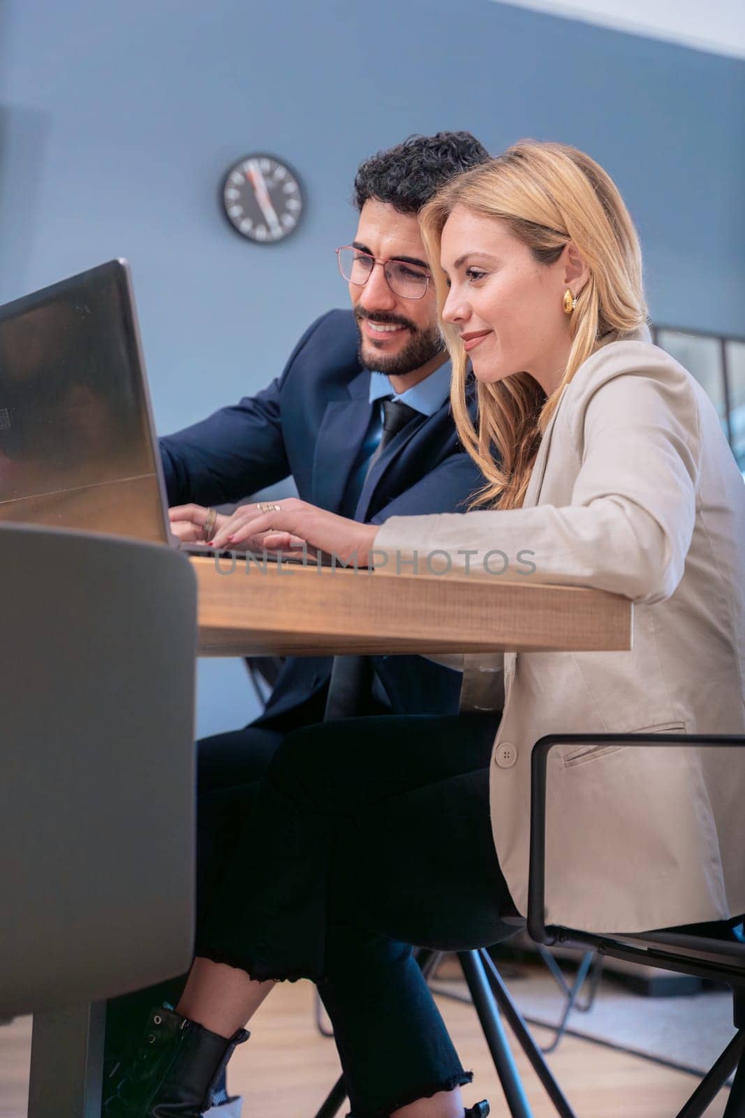 Two business colleagues collaborate in a modern office, smiling as they work together on a laptop. They share ideas in a professional yet friendly environment, fostering productivity and teamwork.