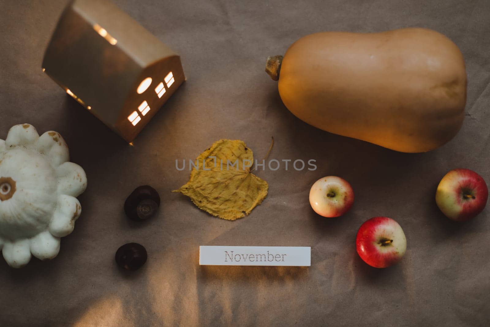 Cozy autumn composition with paper house surrounded by autumn leaves, candles and pumpkin top view. Hygge home decor. Halloween and Thanksgiving concept.
