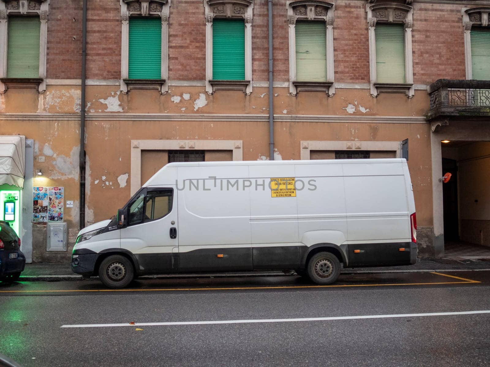 Cremona, Lombardy, Italy October 15th 2024 White delivery van parked on a city street with an old, weathered building in the background