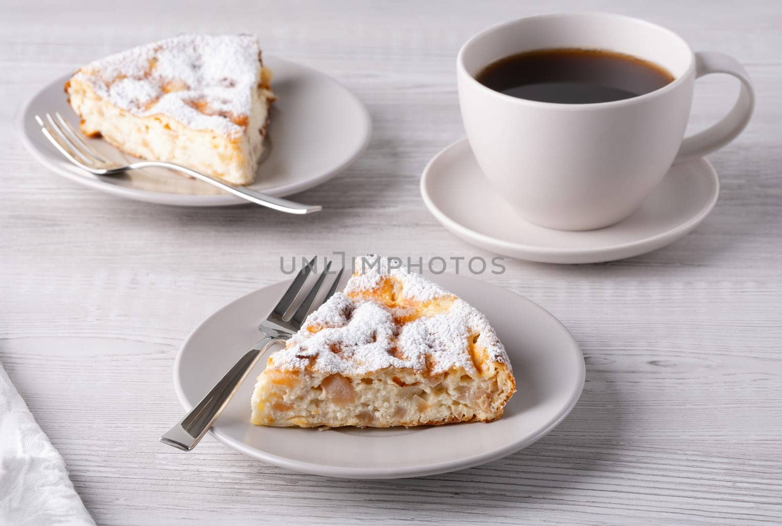 Two delicious pieces of cottage cheese casserole and coffee on a light wooden table.
