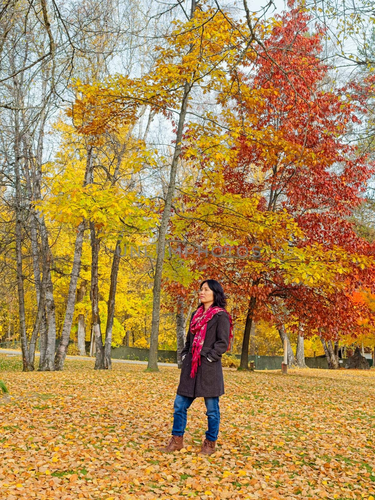 A woman in a stylish coat and a red scarf strolls through a beautiful park in autumn in eastern Washington.