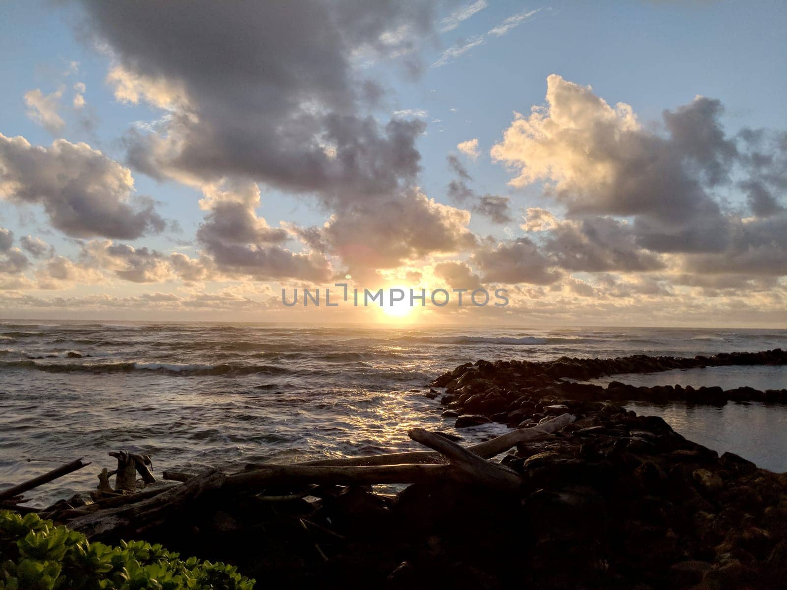 A vibrant sunset illuminates the ocean as colorful clouds drift across the sky, casting a warm glow over the calm waves and rocky shoreline at Lydgate Beach Park.