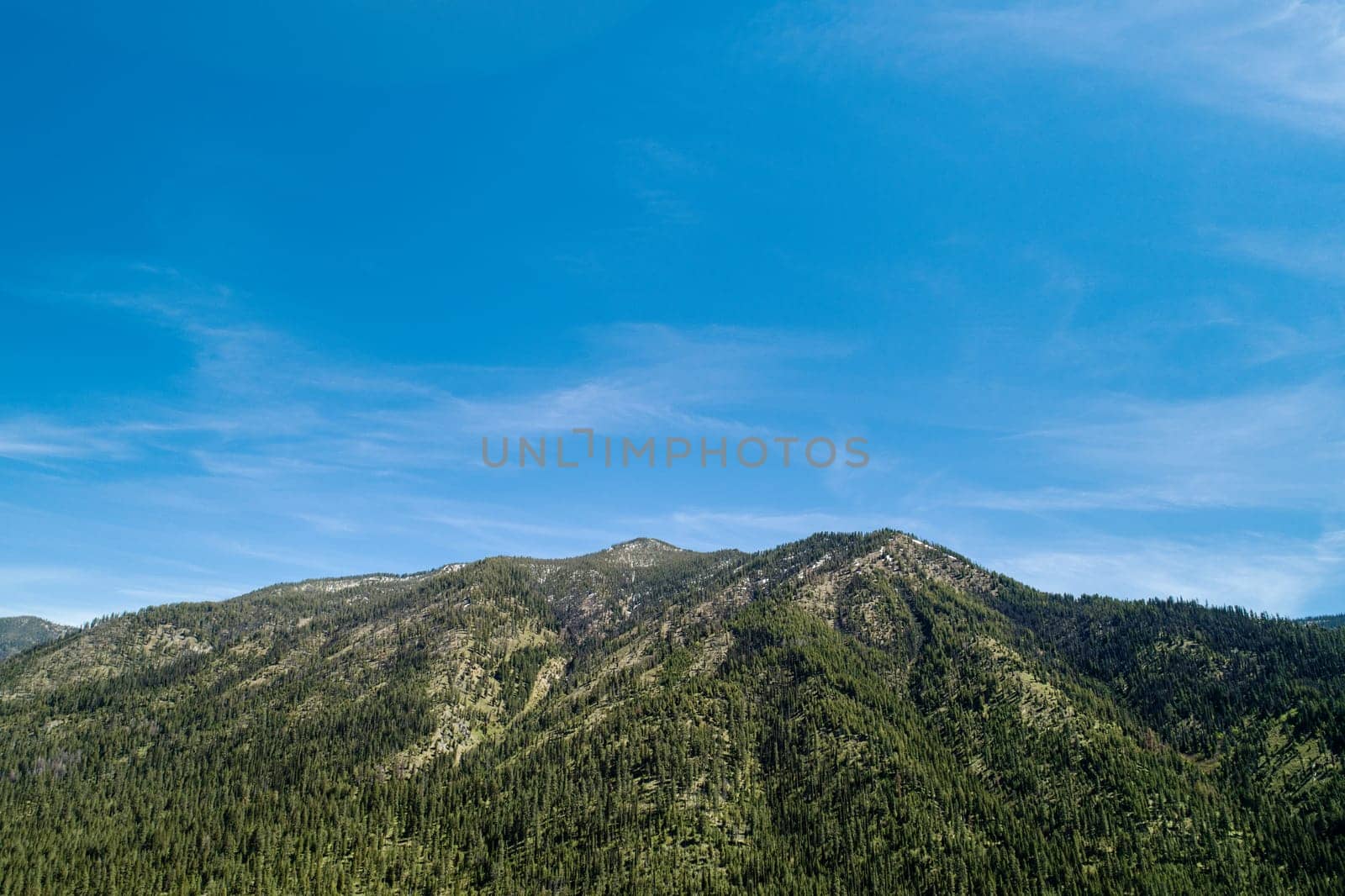 A stunning aerial view of a lush green mountain range beneath a clear blue sky. Perfect representation of tranquil nature, scenic beauty, and outdoor adventure.
