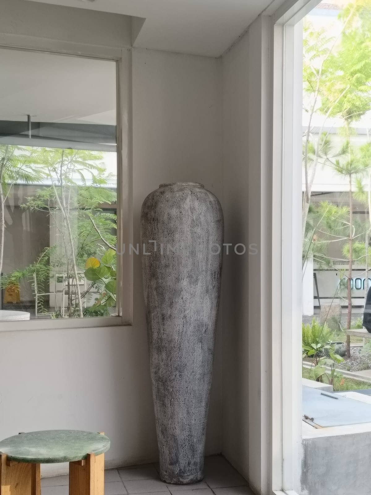 A tall decorative vase adds an artistic touch to a minimalist modern interior. Surrounded by natural light and greenery, this scene exudes tranquility and elegance in contemporary design.